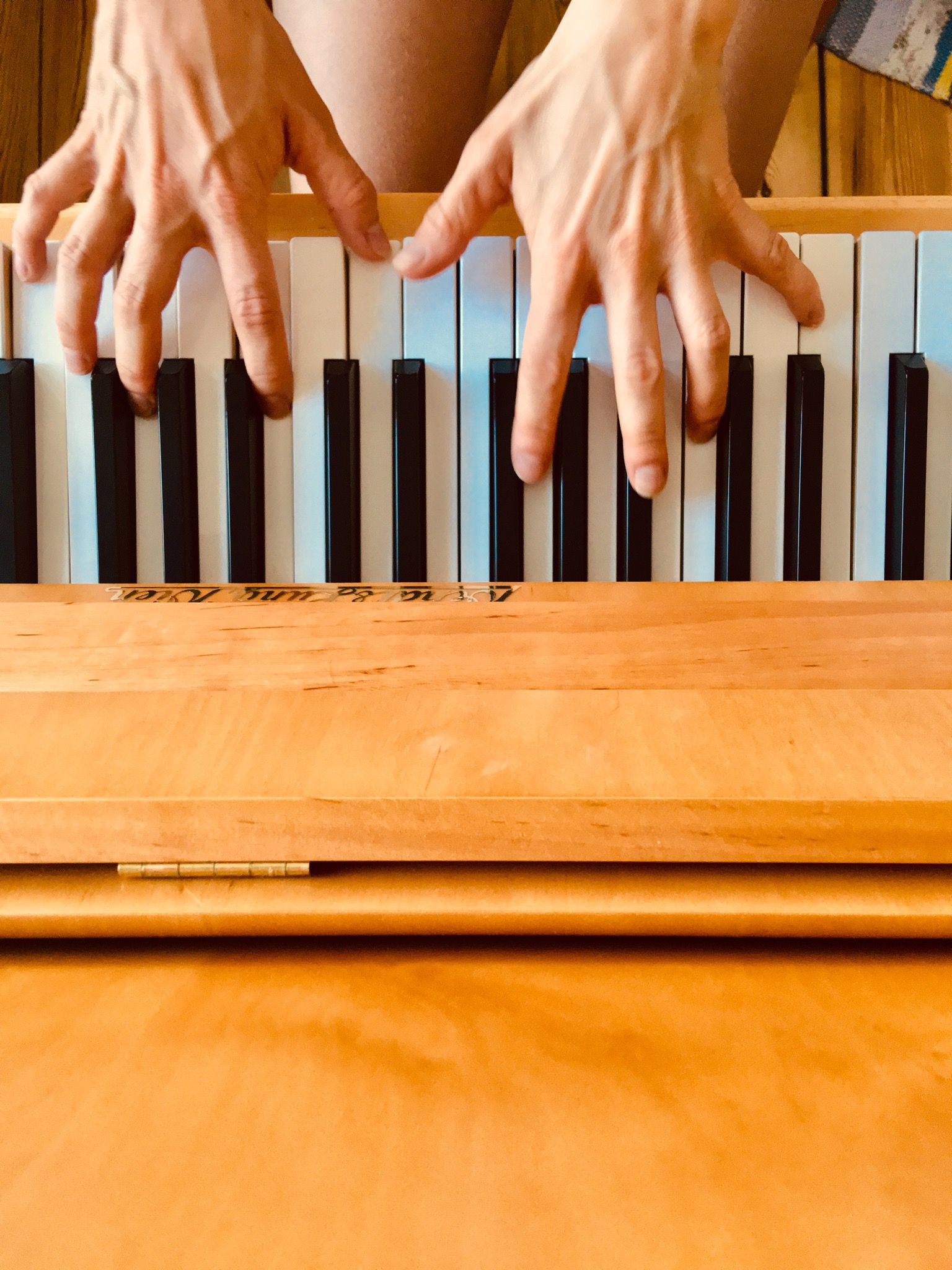 View on a bright wooden piano: the black and white keys are played by two hands